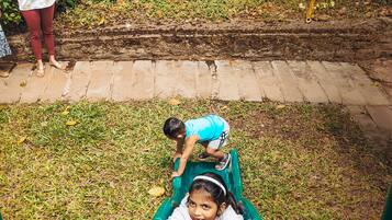 Children can play on the slide in this playground surrounded by lush greenery and a brick wall.