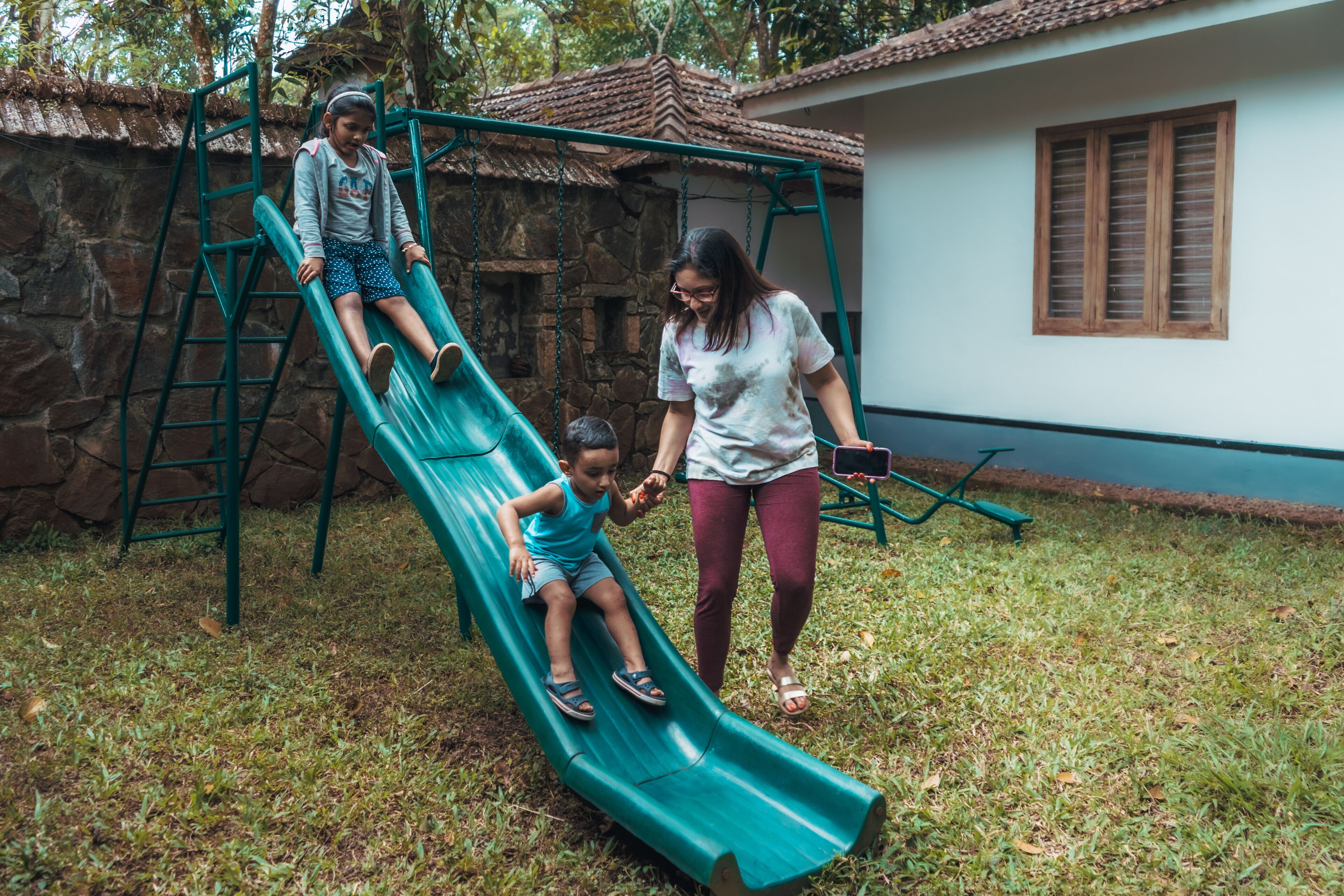 A playground with a green slide and a stone wall in the background.