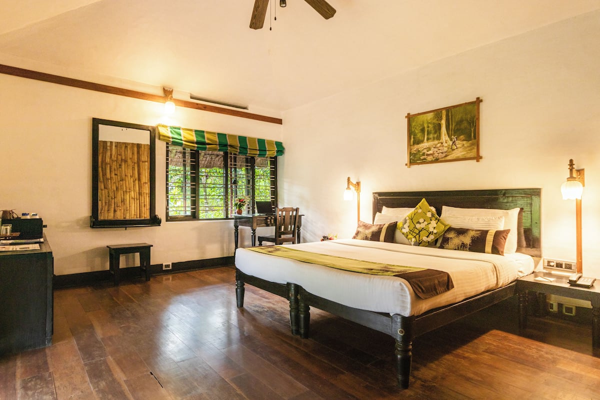 A bedroom with a wooden bed, a desk, a chair, a window with a green and white checkered blind, and a painting on the wall.