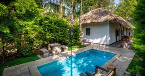 A swimming pool with stone steps leading to a thatched-roof building, surrounded by lush greenery. - Amritara Shalimar Spice Garden Resort & Spa (Peermade)