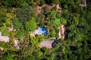 Vista aérea de una propiedad con piscina rodeada de densa vegetación tropical.