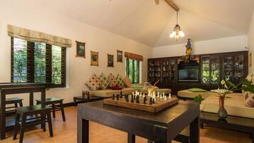 Uma sala de estar acolhedora com um tabuleiro de xadrez, um sofá com almofadas, uma televisão e uma estante de livros.