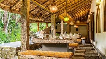 Un comedor al aire libre rústico con mesas y bancos de piedra, rodeado de follaje.