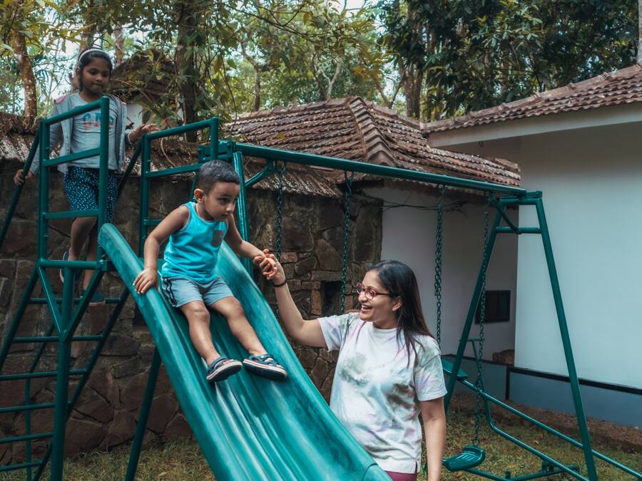 A playground with a green slide, a climbing structure, and a building with a tiled roof in the background.