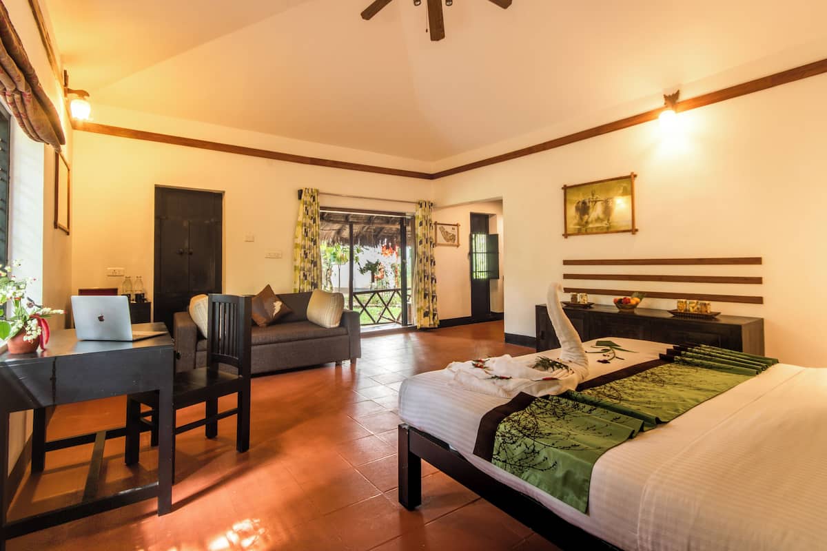 A bedroom with a bed, a desk with a laptop, a chair, a sofa, and a balcony with curtains.