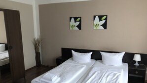 A hotel room with two single beds, a nightstand with a lamp, a vase with dried plants, and two wall-mounted flower paintings. - Hotel-Pension Reiter (Berlin)
