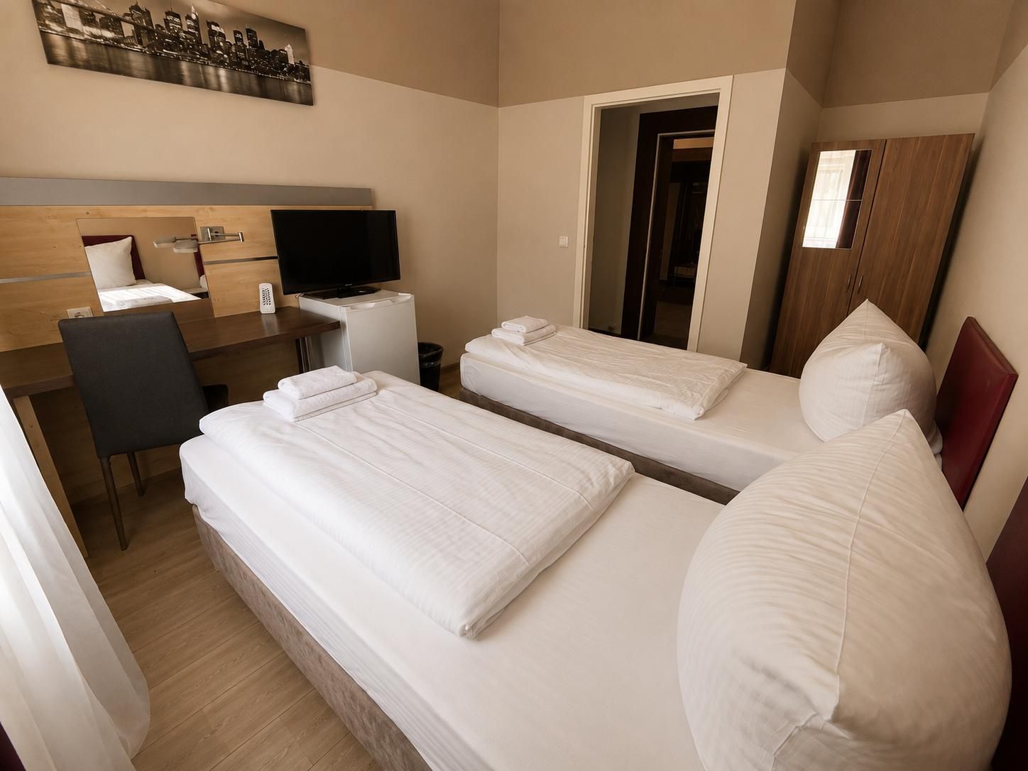 Une chambre d’hôtel avec deux lits, un bureau avec une télévision, une chaise et une porte donnant sur une autre pièce.
