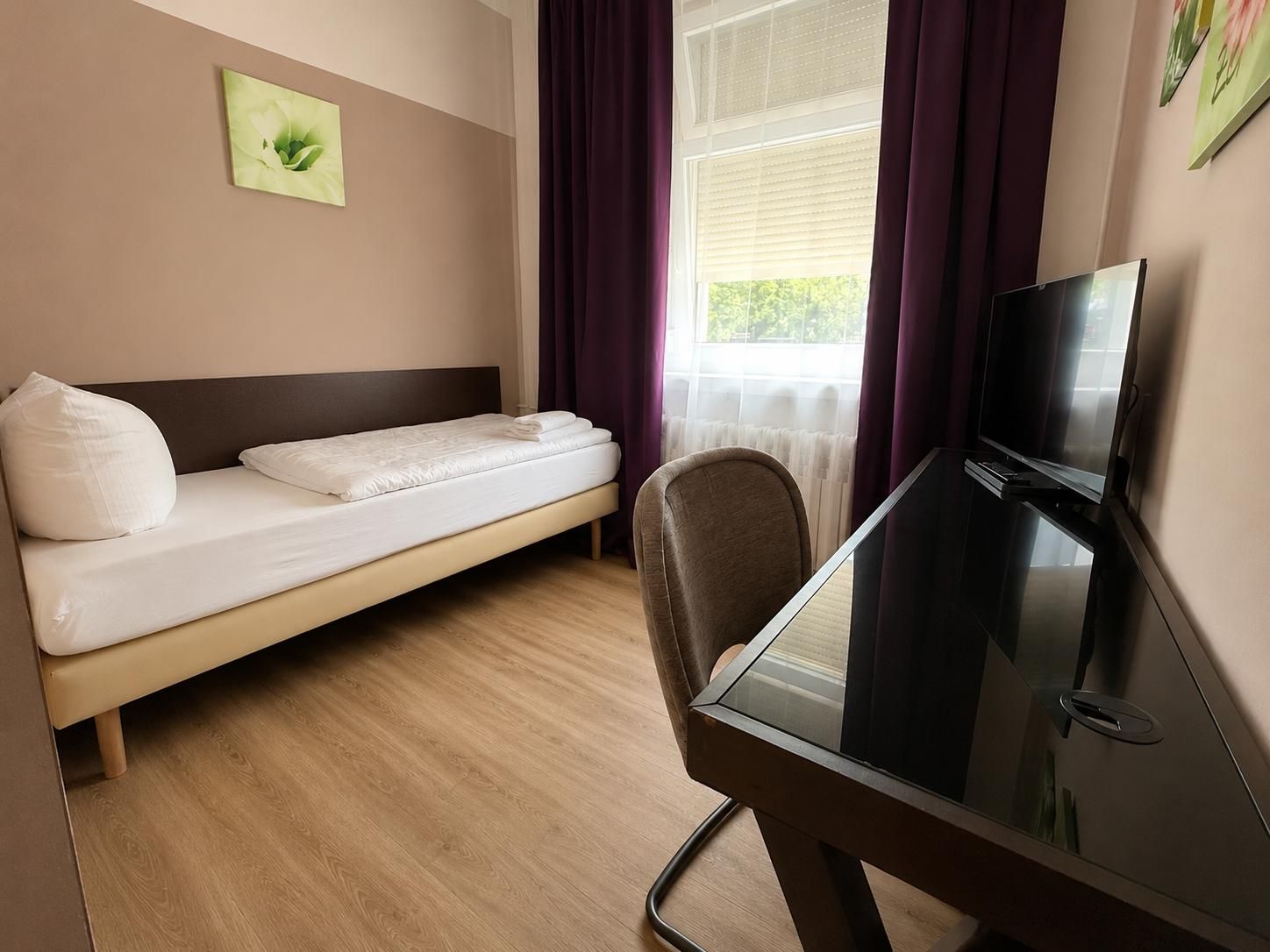 A single bed with a headboard, a television on a stand, and a window with curtains.