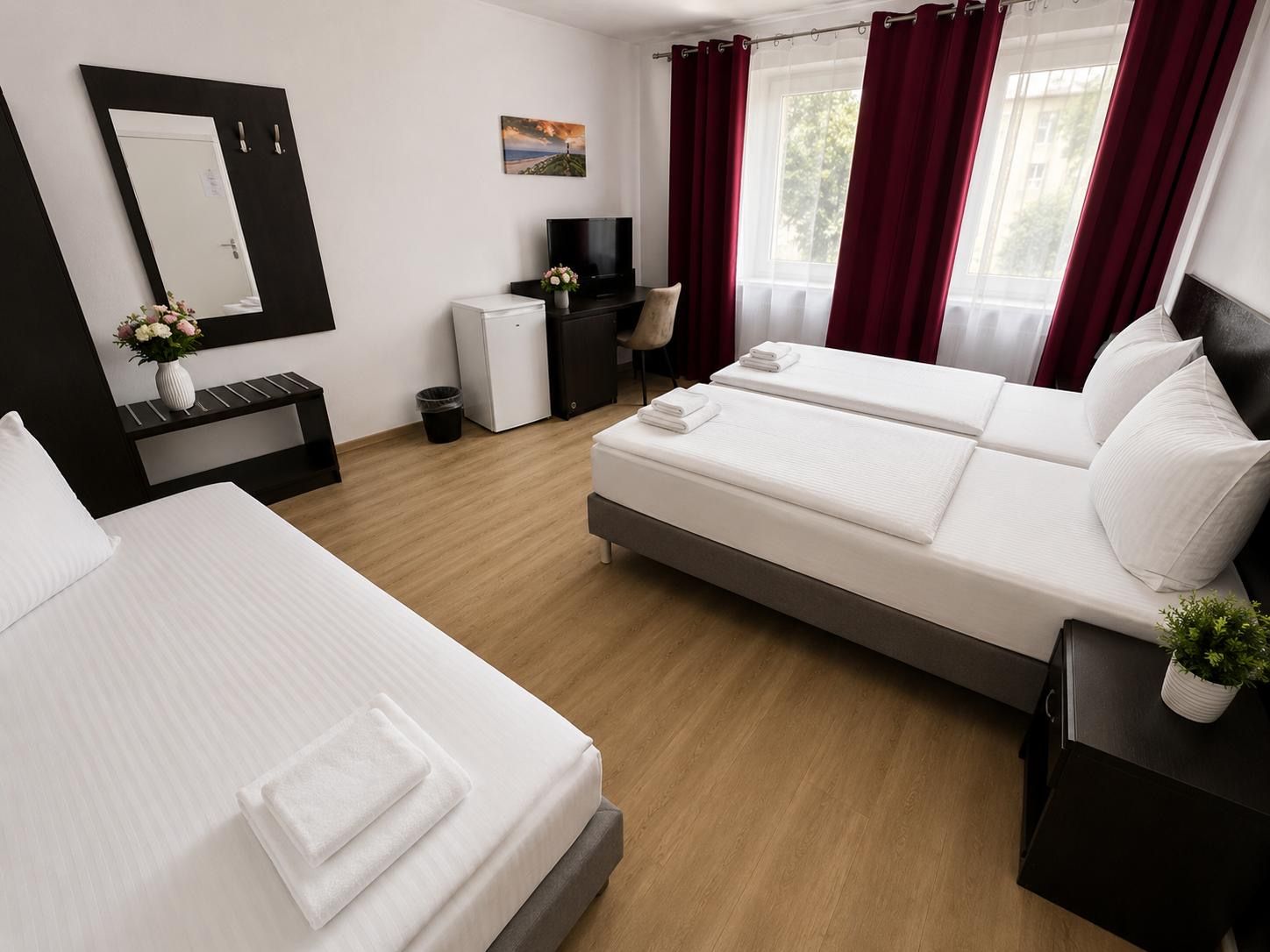 Ein Hotelzimmer mit zwei Betten, einem Schreibtisch, einem Fernseher und einem fenster mit Vorhängen.