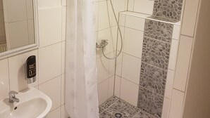 A bathroom with a hand wash station, a shower with a stone tile accent, and a mirror. - Hotel-Pension Reiter (Berlin)