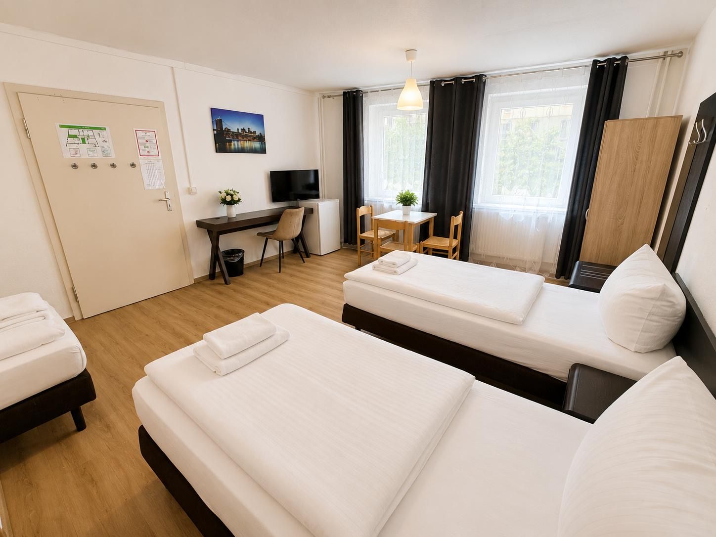 Ett hotellrum med två sängar, ett skrivbord, en tv, ett litet bord med en växt och ett fönster med gardiner.
