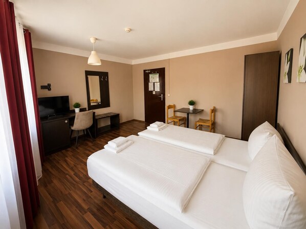 Ein Hotelzimmer mit einem Bett, einem Schreibtisch mit Stuhl, einem Fernseher und einem kleinen Tisch mit Sitzgelegenheiten.