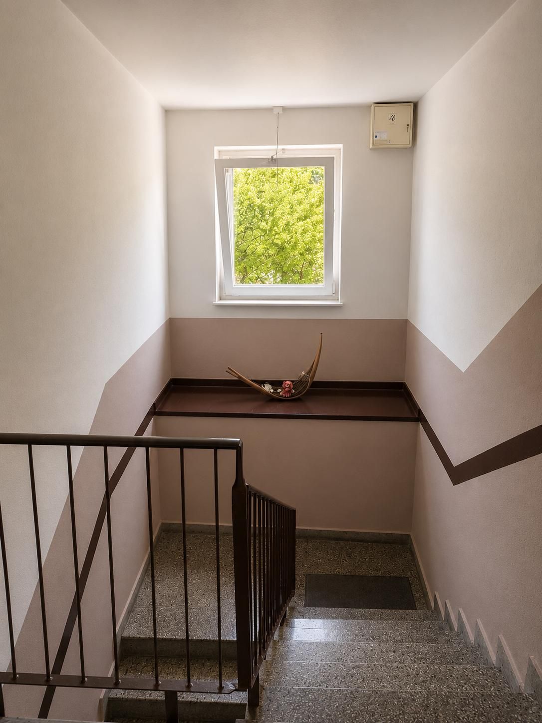Una escalera con ventanal, un estante pequeño y barandilla metálica.