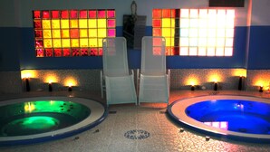 Two hot tubs with tiled floors and chairs in a room with windows. - Hotel Cristina (Rocca San Giovanni)