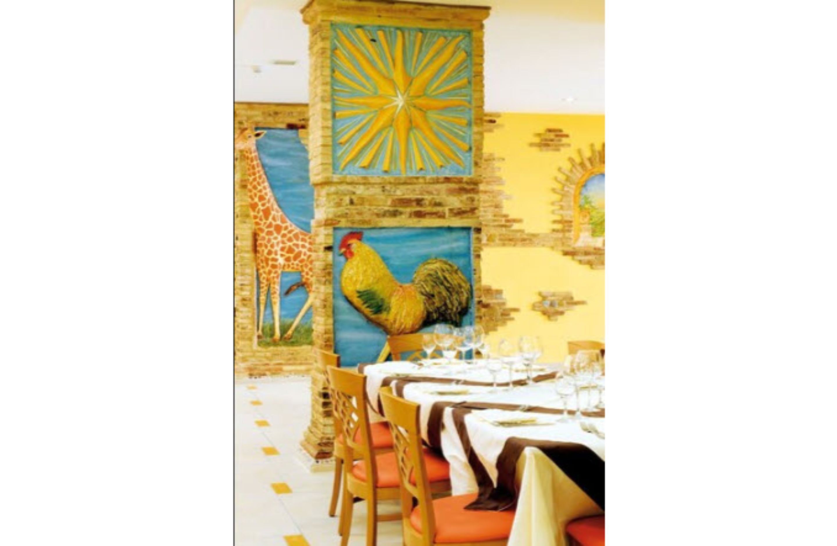 A dining area with a mural of a rooster and a giraffe, wooden chairs, and a table set for a meal.