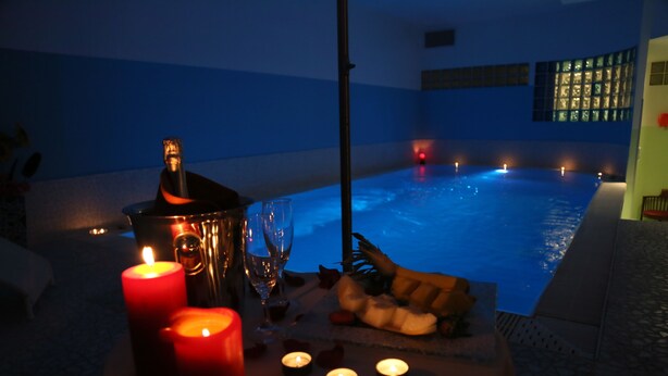 A dimly lit indoor pool area with candles, a bottle, and a fruit platter. - Hotel Cristina (Rocca San Giovanni)