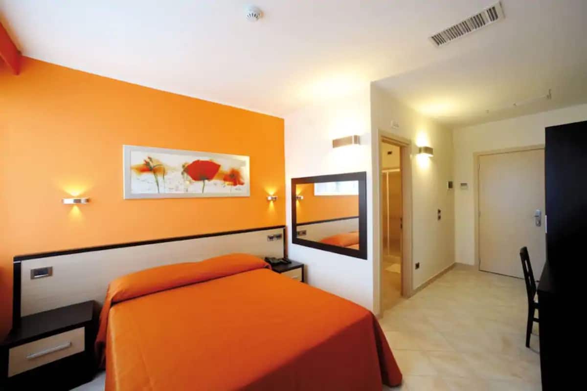 Une chambre d’hôtel avec un lit, une table de chevet, un miroir et un tableau au mur.