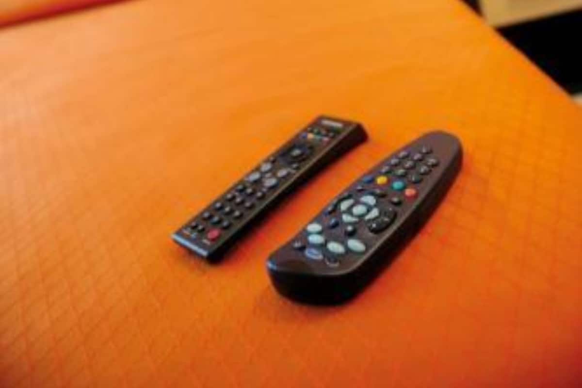 Un lit avec une couvre-lit orange et deux télécommandes posées dessus.