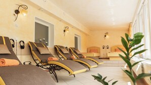 Une salle de spa équipée de plusieurs chaises longues, d’un lit et d’une fenêtre agrémentée de plantes.