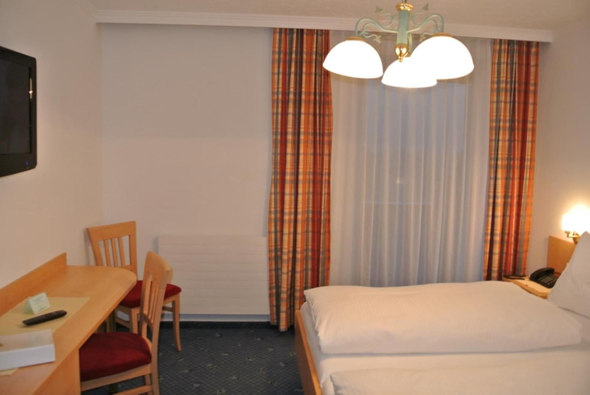 A hotel room with a bed, a desk with a chair, a telephone, and a television.