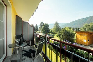 Un balcon avec une table et des chaises, une clôture en bois et une vue sur un paysage verdoyant, avec des arbres et une montagne en arrière-plan.