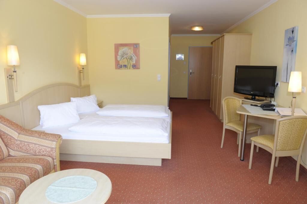 A hotel room with a bed, a desk with a television, a chair, and a couch.