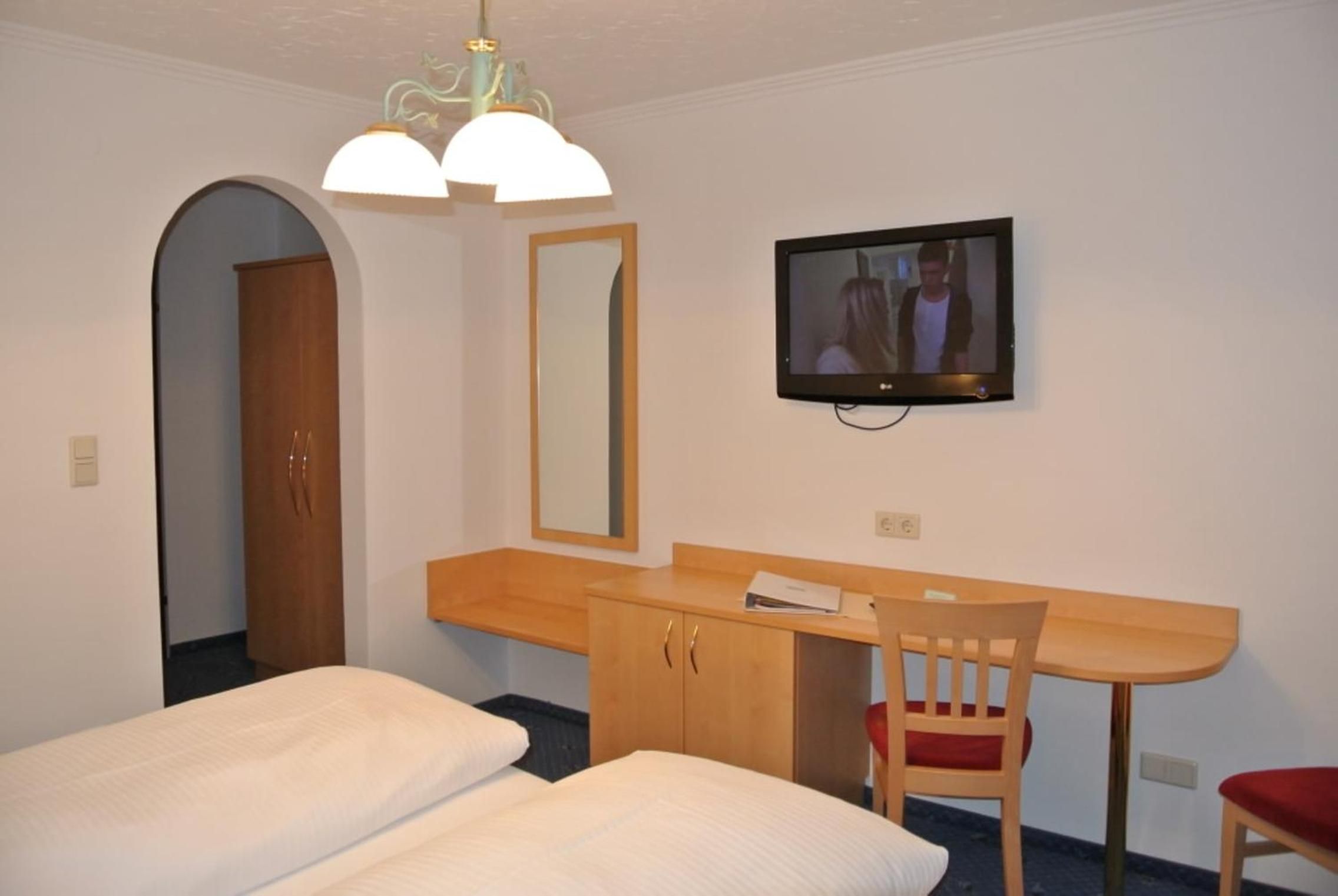 Une chambre d’hôtel équipée d’un lit, d’un bureau, d’une chaise, d’une télévision et d’un miroir.