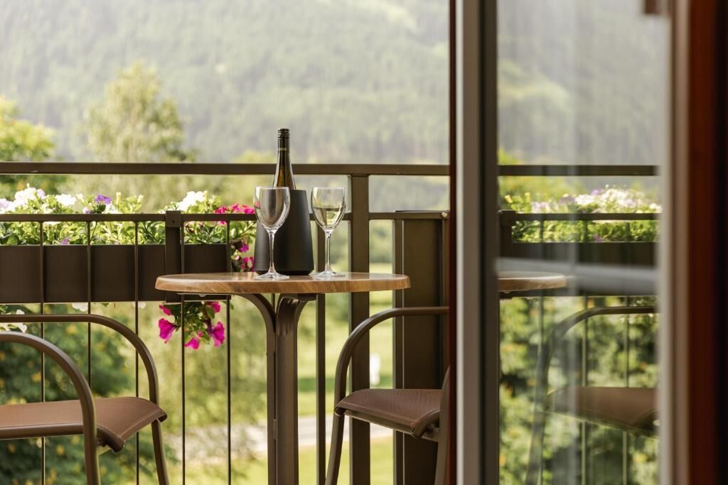 Ein Balkon mit Tisch, zwei Stühlen, einer Flasche und zwei Gläsern.