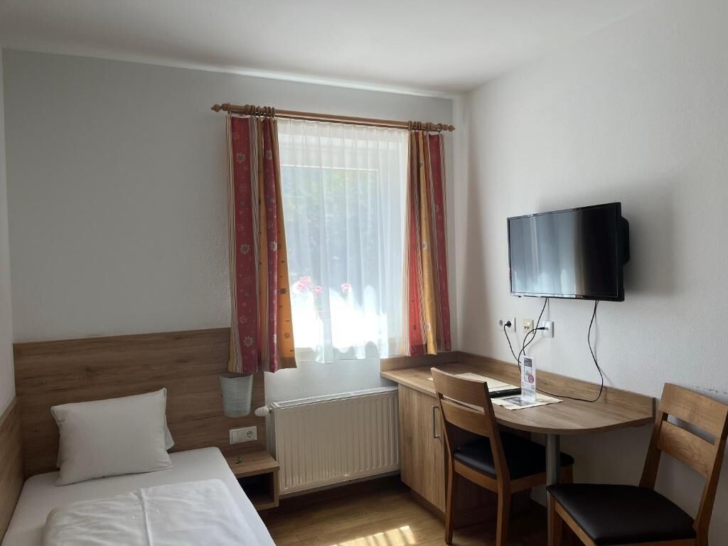 Habitación de hotel con cama, escritorio, silla, televisor y ventana con cortinas.