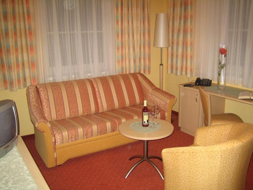 A hotel room with a sofa, a small round table, a lamp, a telephone, and a decorative vase with a flower.