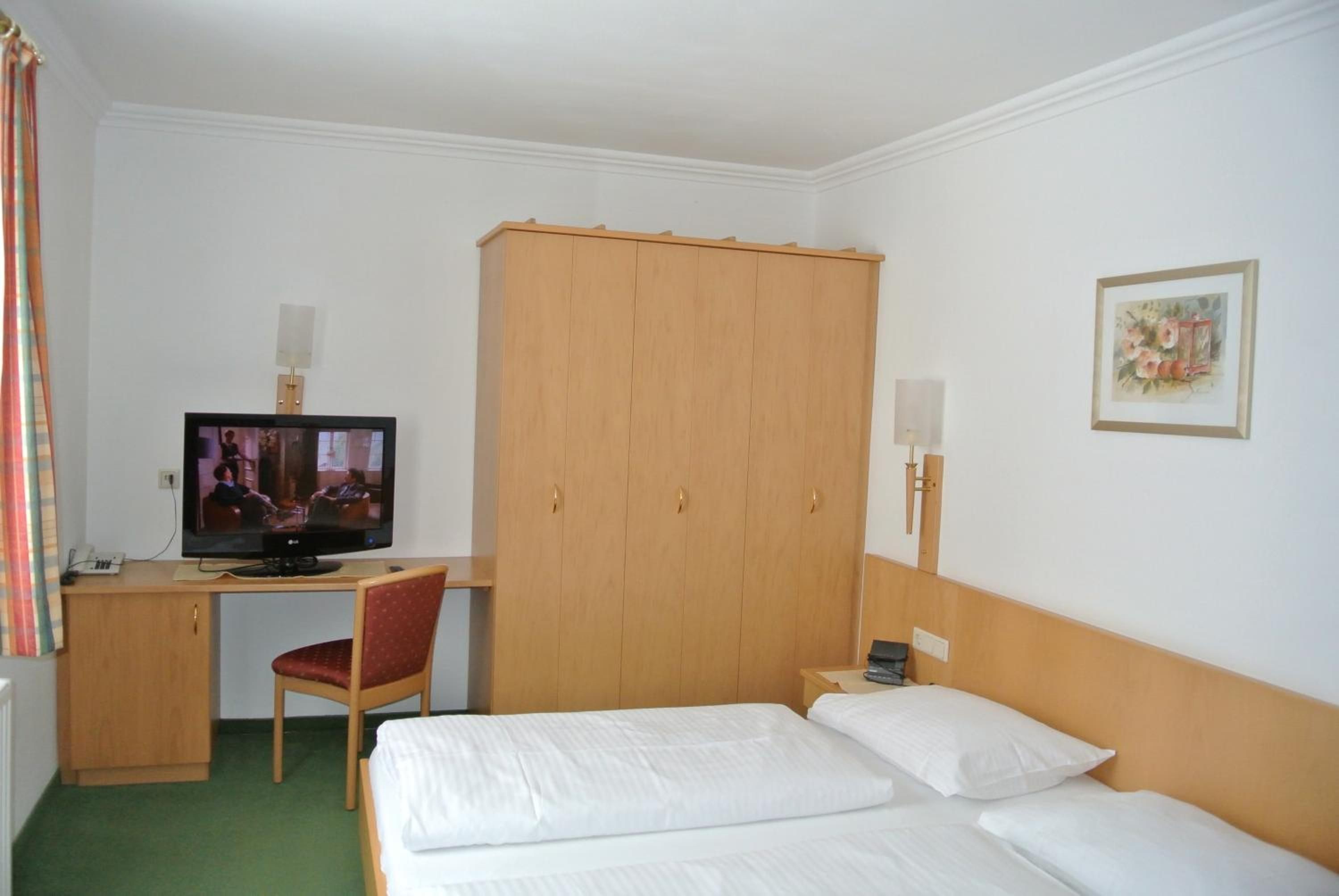 A hotel room with a bed, a desk with a computer, a television, and a wardrobe.