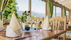 Une table dressée pour le dîner, avec vue sur les montagnes, des chaises en bois et un vase rempli de fleurs.