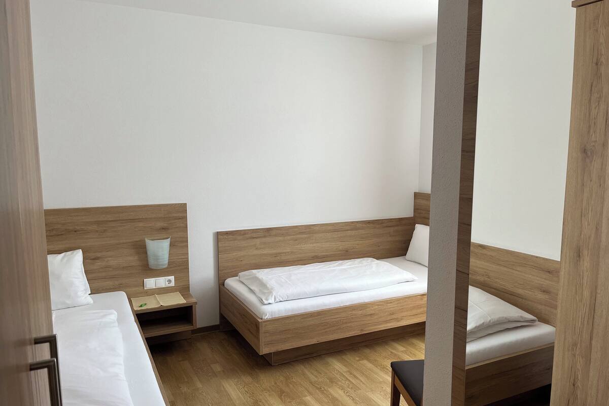 Habitación de hotel con dos camas, cabeceros de madera, ropa de cama blanca, una mesita de noche con lámpara y suelo de madera.