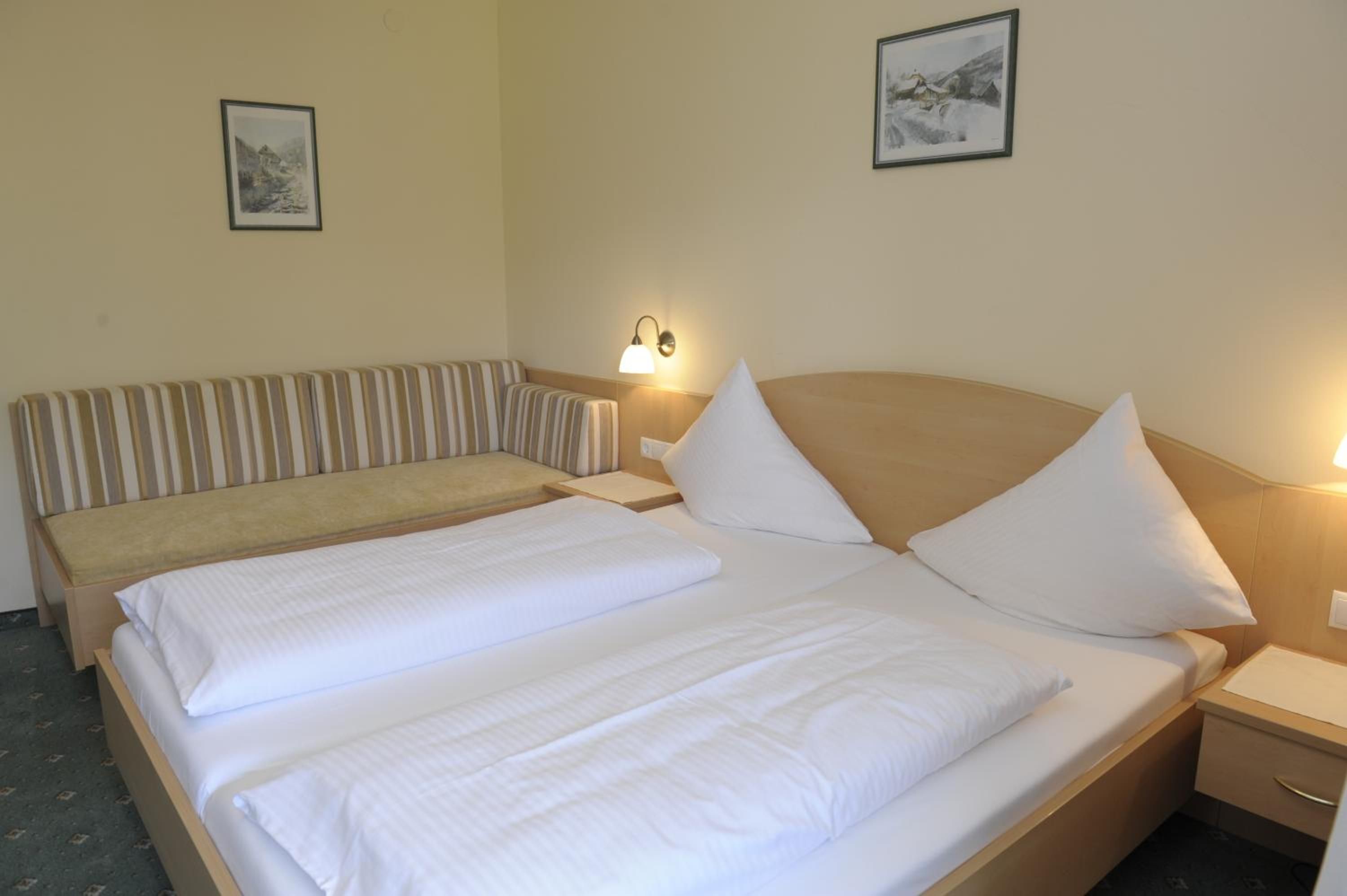 A hotel room with a large bed, a smaller bed, a bedside table, a lamp, and two framed pictures on the wall.
