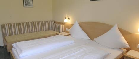 A hotel room with a large bed, a smaller bed, a bedside table, a lamp, and two framed pictures on the wall.
