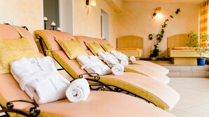 Une rangée de chaises longues avec des serviettes, une plante en pot et des lampes fixées au mur, le tout dans un décor évoquant un spa.