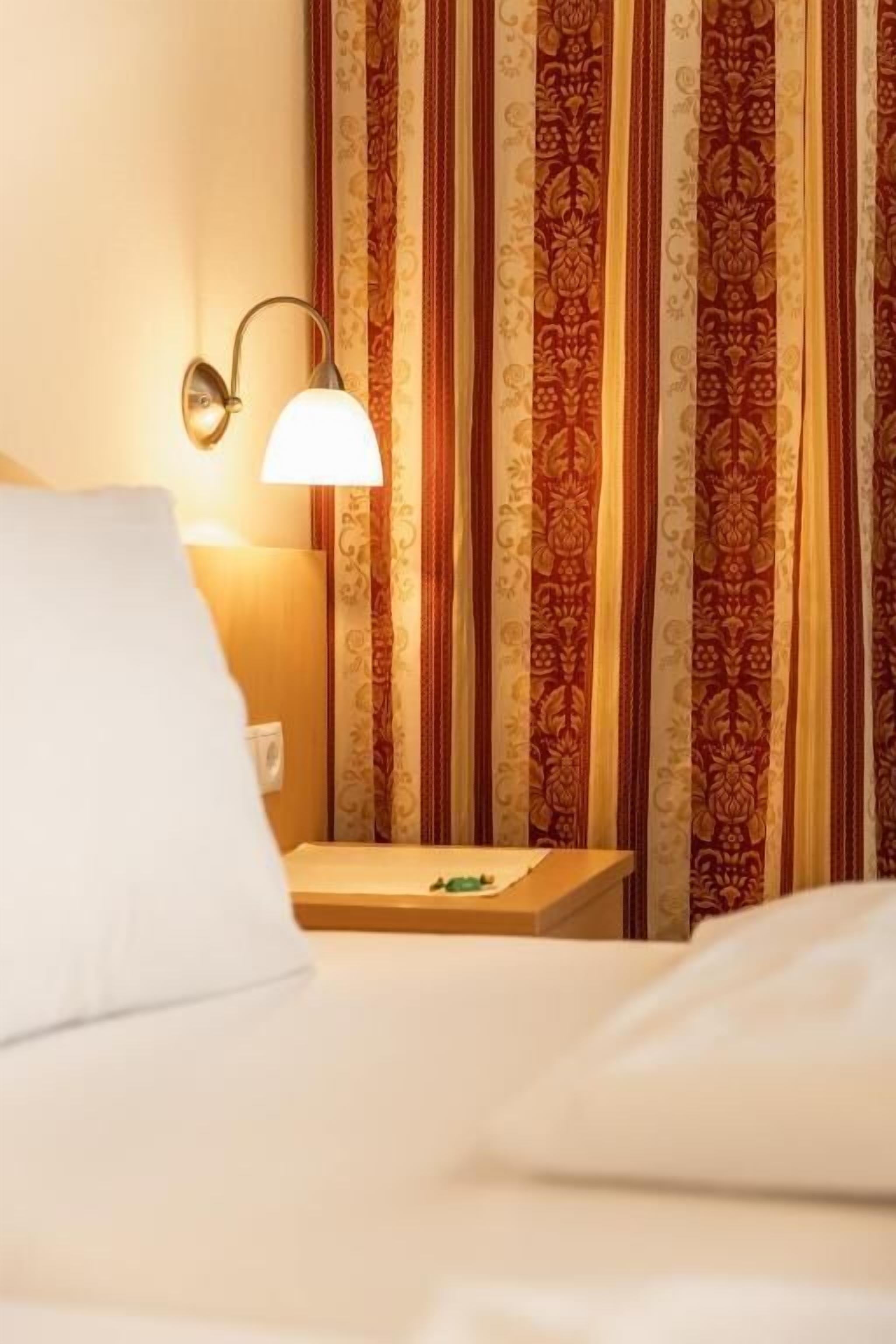 Una habitación de hotel con cama, mesita de noche, lámpara y cortinas con diseño estampado.