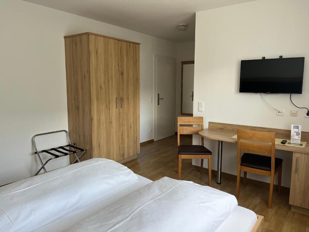 Quarto de hotel com uma cama, escrivaninha com cadeira, televisão e guarda-roupa.