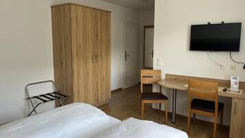 Quarto de hotel com uma cama, escrivaninha com cadeira, televisão e guarda-roupa.