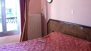A bedroom with a bed, a window with curtains, a radiator, and a wall-mounted light fixture. - Hôtel De Lorraine (Paris)