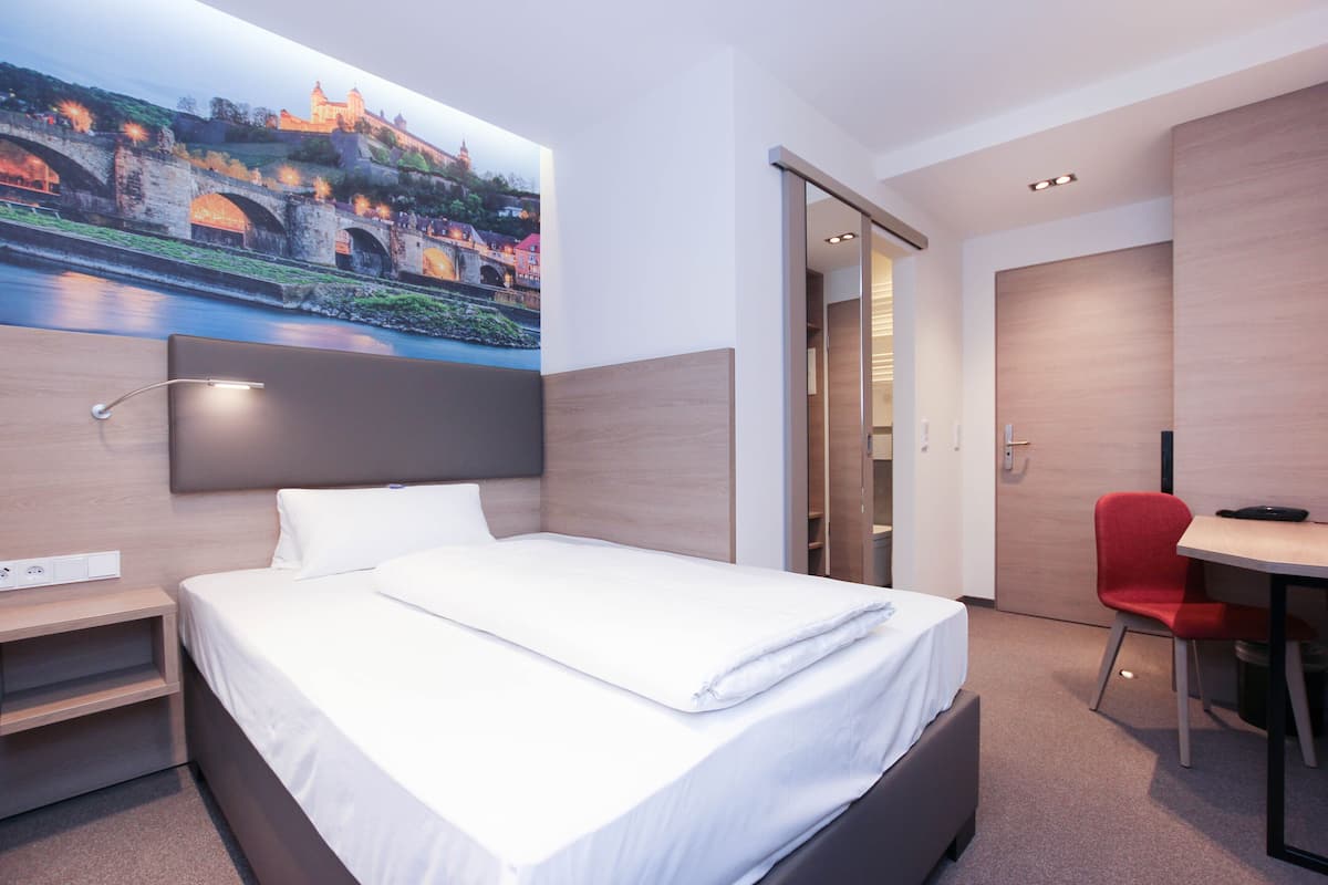 A modern hotel room with a neatly made bed, a desk, and a chair.