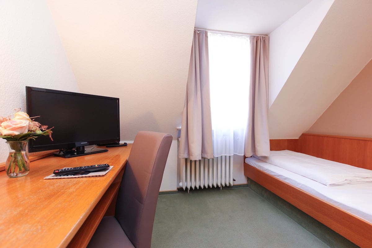 A hotel room with a wooden desk, a television, a chair, a bed, and a radiator.