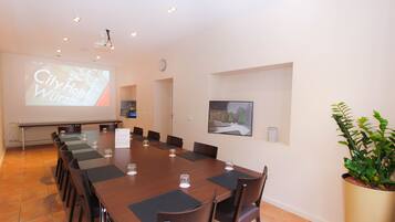 A conference room with a long table, chairs, a projector screen, and a clock on the wall.