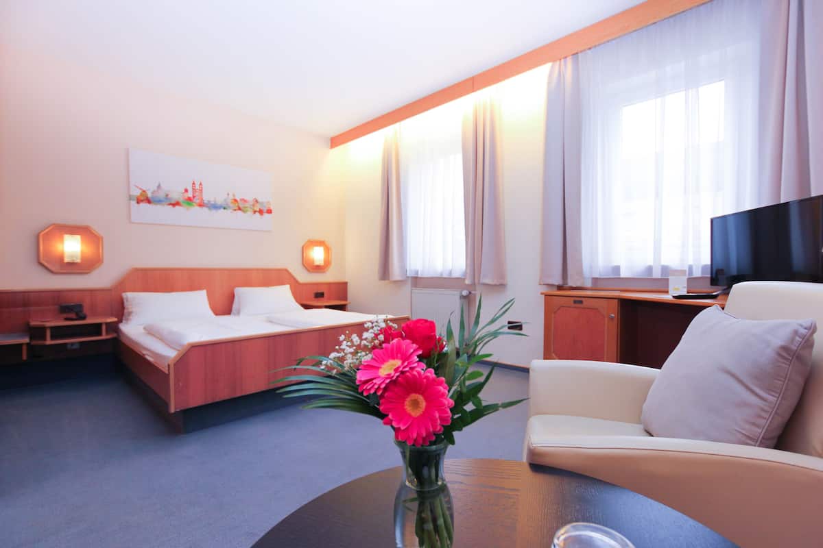 A hotel room with a bed, a desk, a TV, and a vase with flowers.