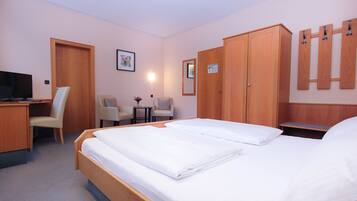 Una habitación de hotel con cama, escritorio, silla, televisor y armario.