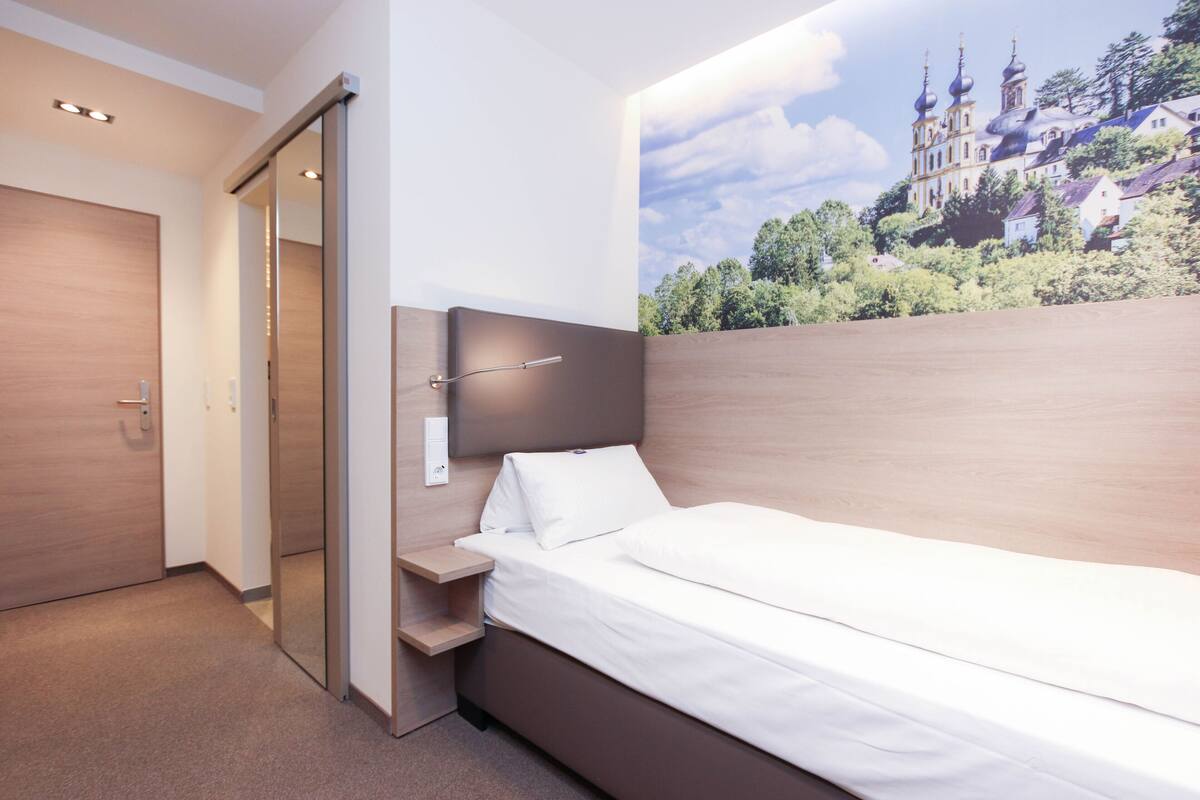 A modern bedroom with a large bed, a wooden headboard, a nightstand, and a sliding door leading to a closet.
