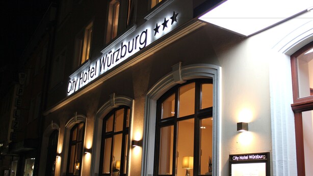 The exterior of City Hotel Würzburg with illuminated signage and large windows. - City Hotel Würzburg (Würzburg)