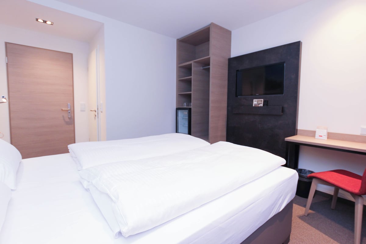 A hotel room with a bed, a desk, a chair, and a TV mounted on the wall.