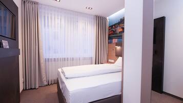 Ein Hotelzimmer mit einem Bett, Vorhängen, einem an der Wand befestigten Fernseher und einem Gemälde einer Brücke.