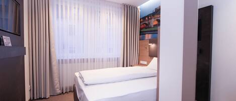 Quarto de hotel com cama, cortinas, televisão presa à parede e pintura de uma ponte.